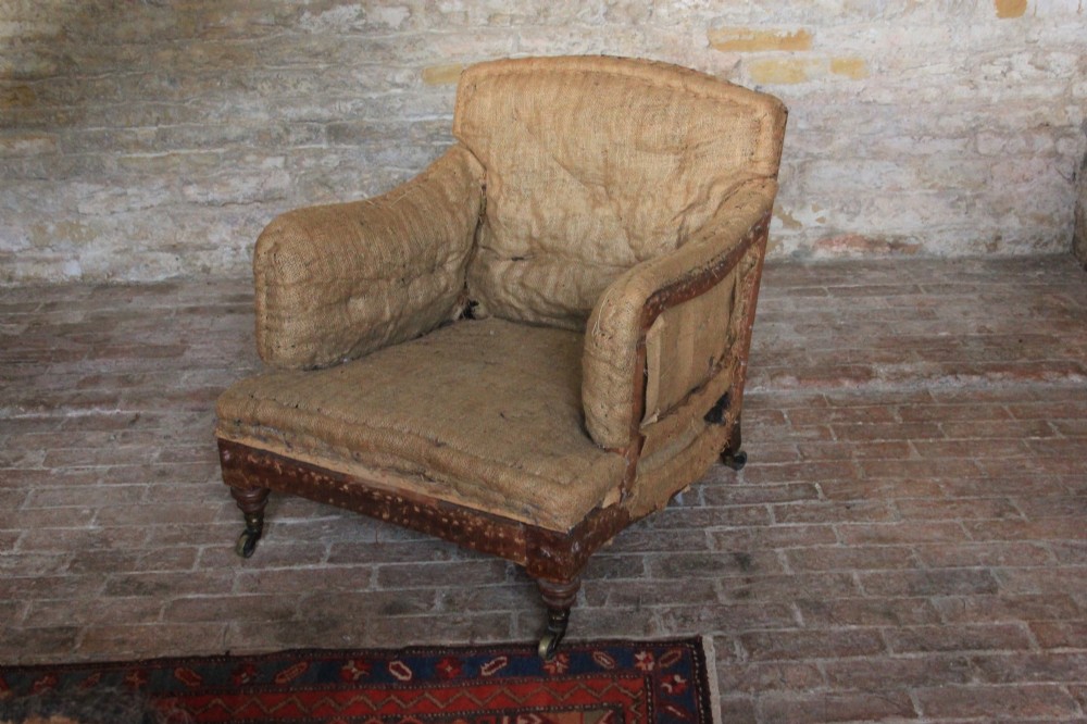 An antique Howard and Sons Bridgewater armchair stripped to its natural hessian upholstery layer with turned timber front legs and brass castors.