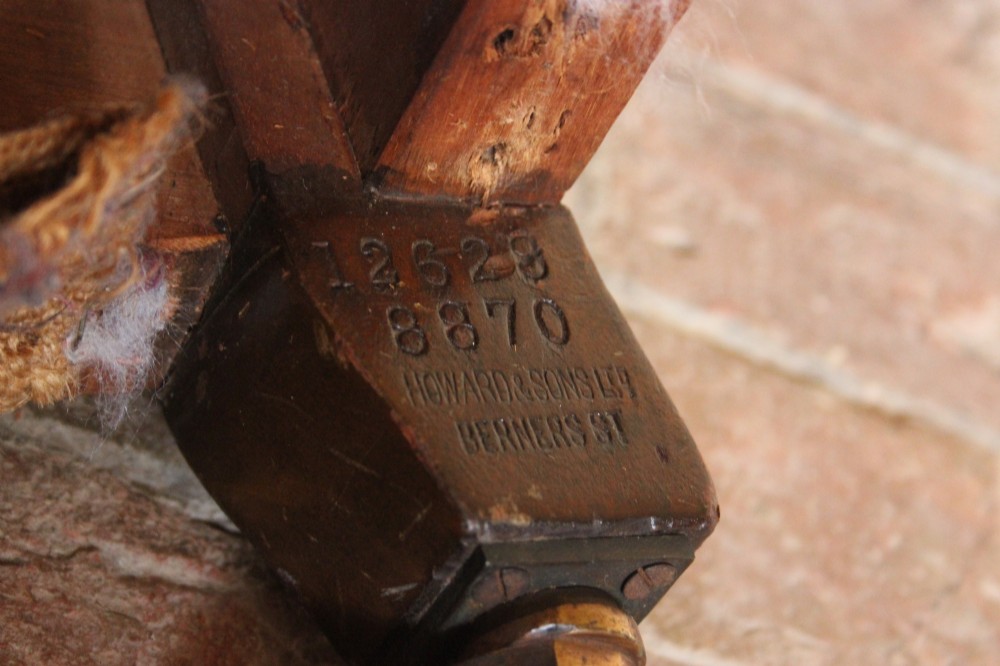 An antique Howard and Sons Bridgewater armchair stripped to its natural hessian upholstery layer with turned timber front legs and brass castors. View II