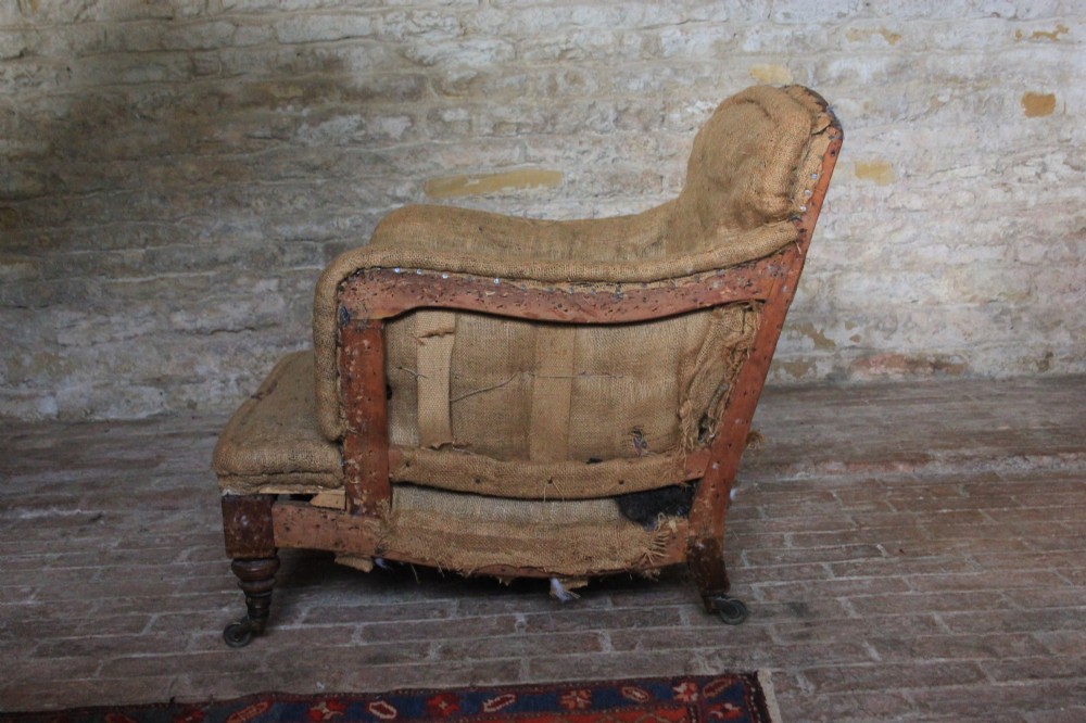 An antique Howard and Sons Bridgewater armchair stripped to its natural hessian upholstery layer with turned timber front legs and brass castors. View IV