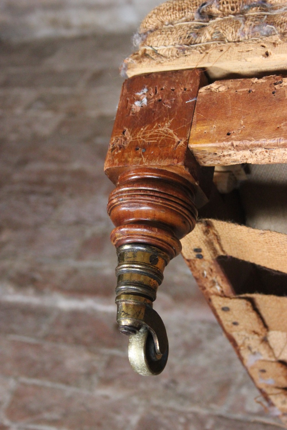 An antique Howard and Sons Bridgewater armchair stripped to its natural hessian upholstery layer with turned timber front legs and brass castors. View V