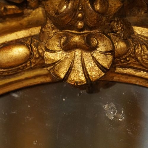 fig 6. An oval giltwood wall mirror featuring a carved pediment crest with scrolling details and a beaded rim.