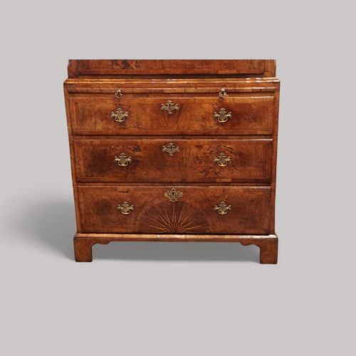 fig 1. A George II walnut tallboy featuring stacked drawers with decorative brass handles, bracket feet, and a sunburst motif on the bottom drawer.