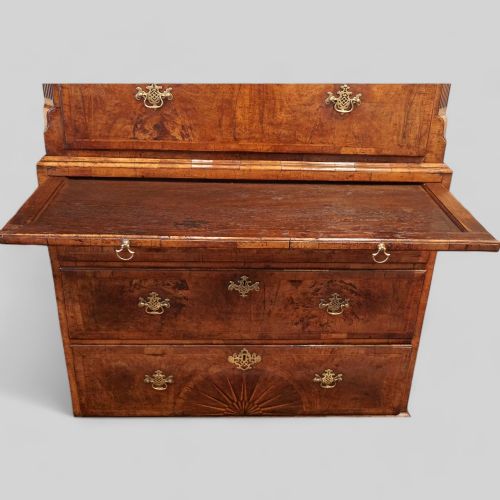 fig 2. A George II walnut tallboy featuring stacked drawers with decorative brass handles, bracket feet, and a sunburst motif on the bottom drawer.