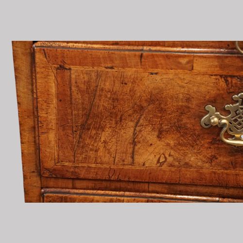 fig 3. A George II walnut tallboy featuring stacked drawers with decorative brass handles, bracket feet, and a sunburst motif on the bottom drawer.