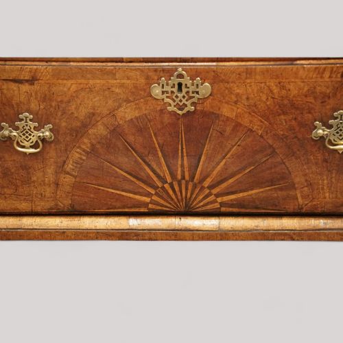 fig 8. A George II walnut tallboy featuring stacked drawers with decorative brass handles, bracket feet, and a sunburst motif on the bottom drawer.