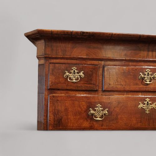 fig 9. A George II walnut tallboy featuring stacked drawers with decorative brass handles, bracket feet, and a sunburst motif on the bottom drawer.