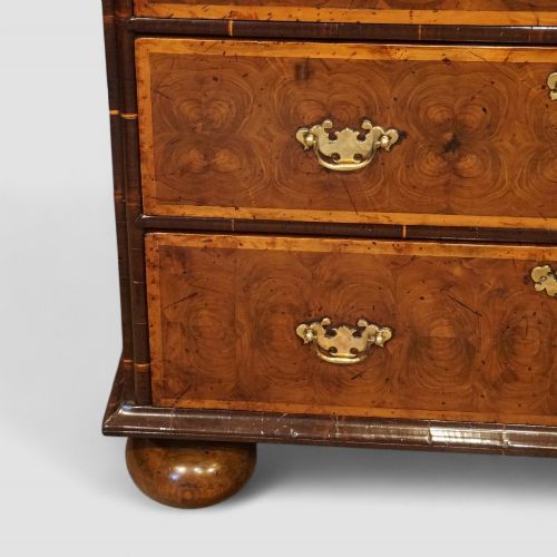 fig 4. A William and Mary period chest of drawers with oyster laburnum veneer, brass handles, and turned bun feet.