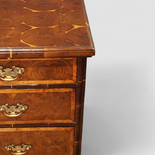 fig 6. A William and Mary period chest of drawers with oyster laburnum veneer, brass handles, and turned bun feet.