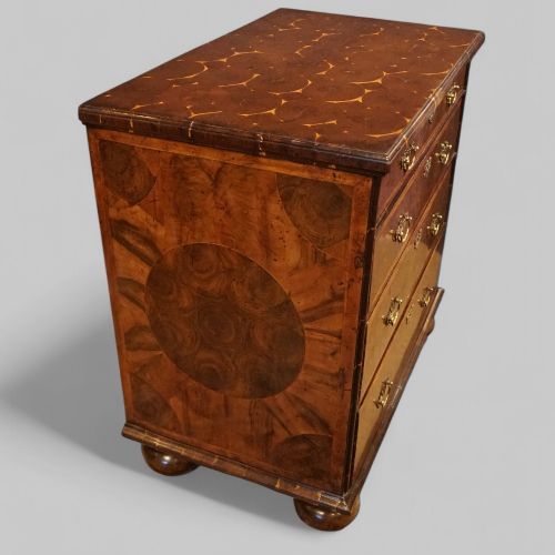 fig 7. A William and Mary period chest of drawers with oyster laburnum veneer, brass handles, and turned bun feet.