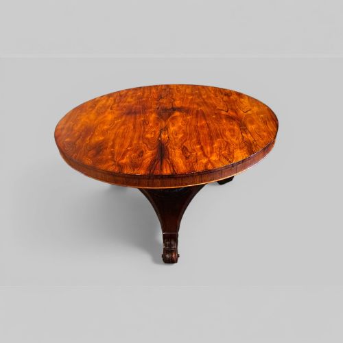 fig 6. A circular antique rosewood dining table with a highly figured timber top shown upright above a carved tri-form pedestal base.
