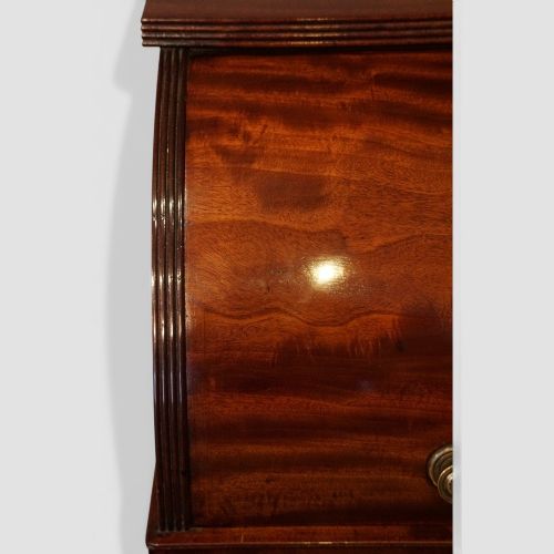 fig 2. An early nineteenth-century mahogany cylinder desk featuring a curved roll-front cover, brass knobs, a long frieze drawer, and turned reeded legs with brass castors.