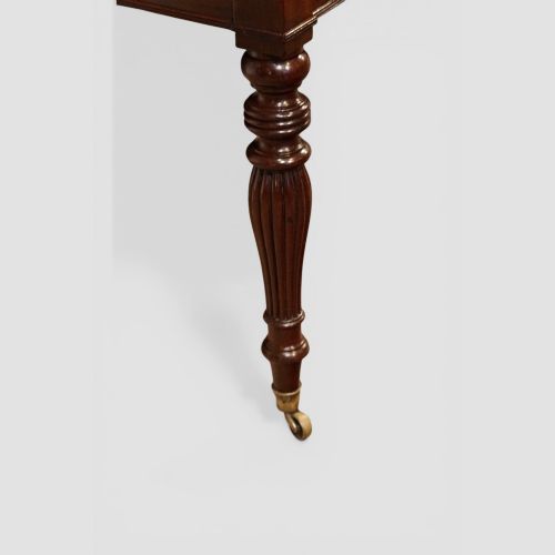 fig 3. An early nineteenth-century mahogany cylinder desk featuring a curved roll-front cover, brass knobs, a long frieze drawer, and turned reeded legs with brass castors.