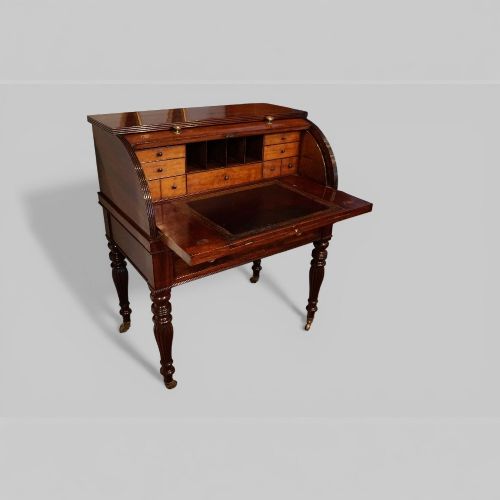 fig 6. An early nineteenth-century mahogany cylinder desk featuring a curved roll-front cover, brass knobs, a long frieze drawer, and turned reeded legs with brass castors.