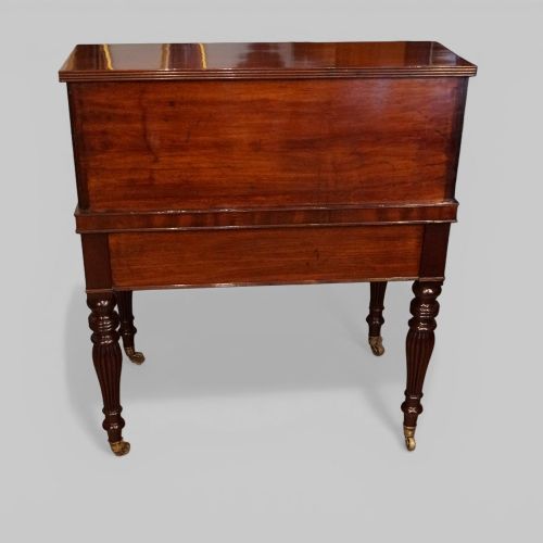 fig 8. An early nineteenth-century mahogany cylinder desk featuring a curved roll-front cover, brass knobs, a long frieze drawer, and turned reeded legs with brass castors.