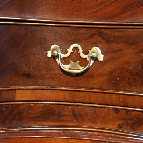 fig 7. A tall George V walnut serpentine front tallboy chest featuring multiple drawers with decorative brass drop handles.