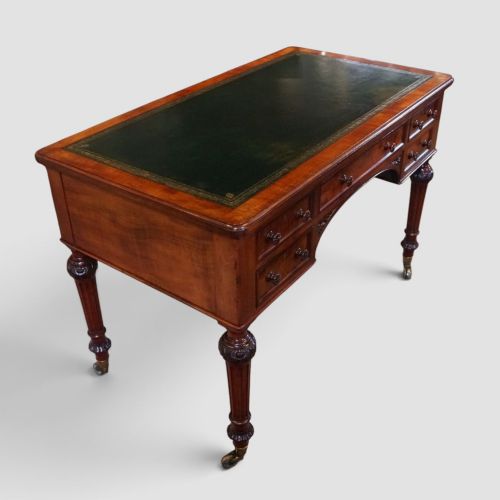 fig 1. Victorian mahogany writing table featuring a dark green leather top, five drawers with circular wooden handles, turned legs, and brass castors.