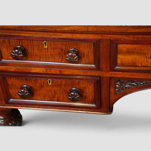 fig 4. Victorian mahogany writing table featuring a dark green leather top, five drawers with circular wooden handles, turned legs, and brass castors.