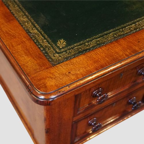 fig 5. Victorian mahogany writing table featuring a dark green leather top, five drawers with circular wooden handles, turned legs, and brass castors.
