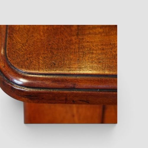 fig 7. Victorian mahogany writing table featuring a dark green leather top, five drawers with circular wooden handles, turned legs, and brass castors.