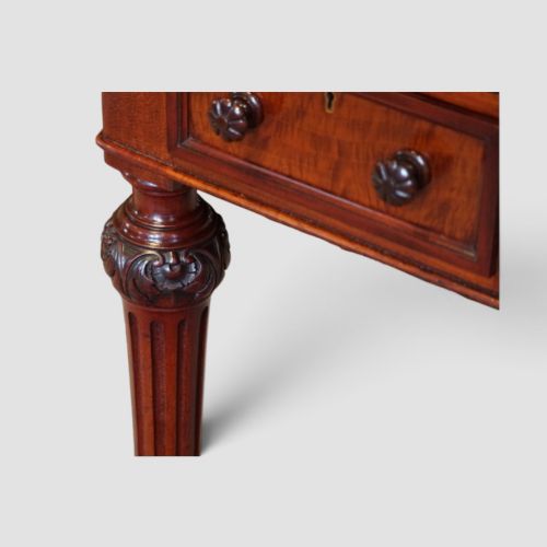 fig 9. Victorian mahogany writing table featuring a dark green leather top, five drawers with circular wooden handles, turned legs, and brass castors.
