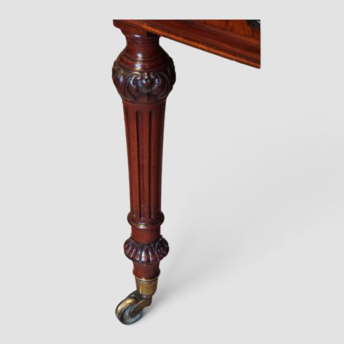 fig 10. Victorian mahogany writing table featuring a dark green leather top, five drawers with circular wooden handles, turned legs, and brass castors.