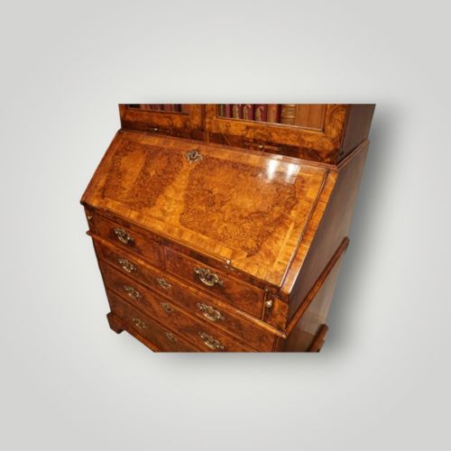 fig 4. A George I walnut bureau bookcase featuring glazed upper doors housing books, a slant-front writing flap, and lower drawers with brass drop handles.