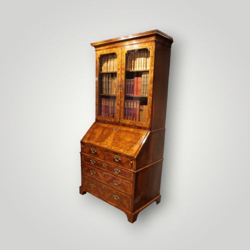 fig 5. A George I walnut bureau bookcase featuring glazed upper doors housing books, a slant-front writing flap, and lower drawers with brass drop handles.