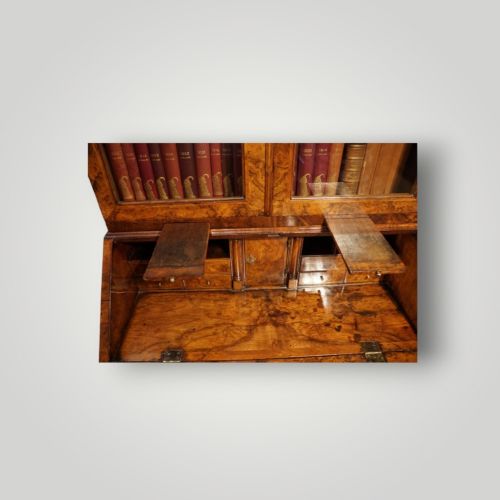 fig 8. A George I walnut bureau bookcase featuring glazed upper doors housing books, a slant-front writing flap, and lower drawers with brass drop handles.
