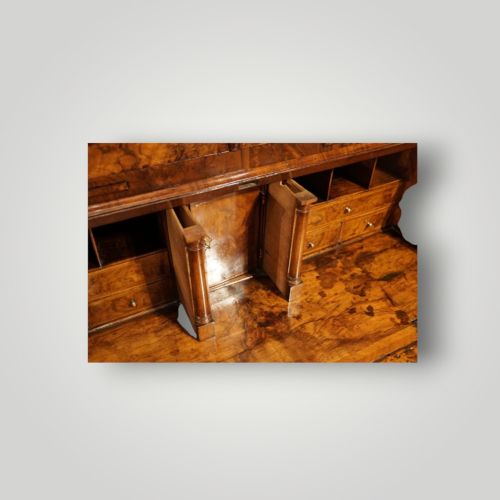 fig 12. A George I walnut bureau bookcase featuring glazed upper doors housing books, a slant-front writing flap, and lower drawers with brass drop handles.