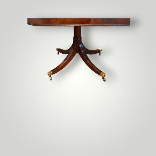 fig 2. A polished mahogany twin pillar dining table featuring rounded corners, two turned central pedestals, and splayed legs resting on brass castors.