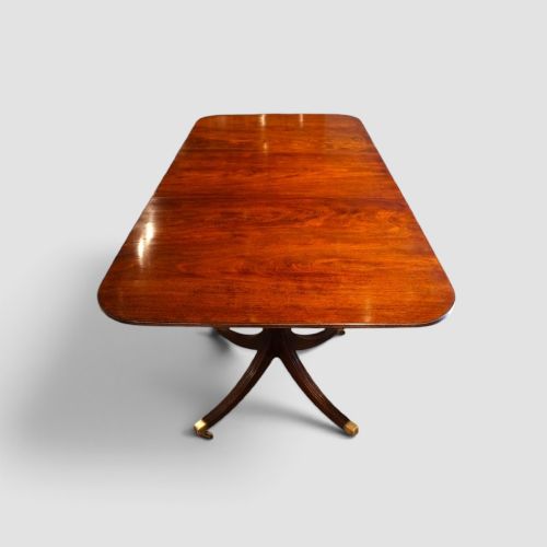 fig 4. A polished mahogany twin pillar dining table featuring rounded corners, two turned central pedestals, and splayed legs resting on brass castors.