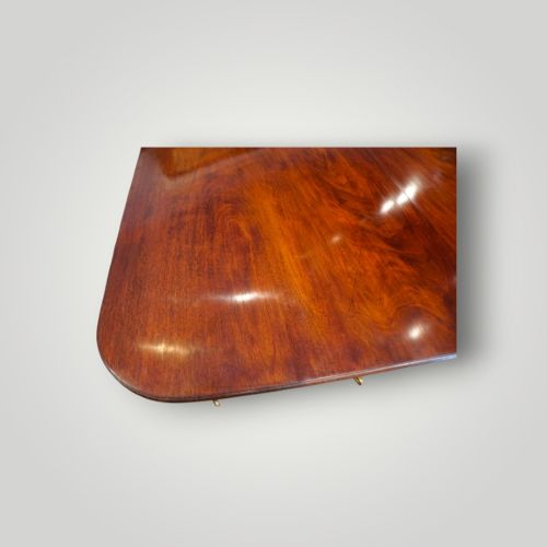 fig 7. A polished mahogany twin pillar dining table featuring rounded corners, two turned central pedestals, and splayed legs resting on brass castors.