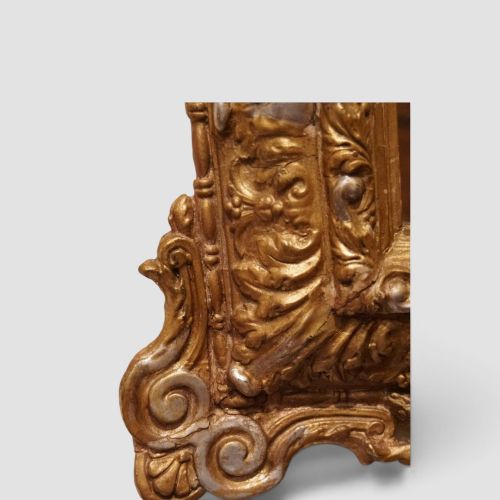 fig 1. An antique trapezoidal wall mirror featuring an ornate giltwood frame with silver-gilt accents, a decorative carved crest, and a tapered profile.