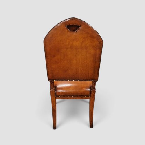 fig 3. A set of four Victorian oak dining chairs featuring arched gothic-style backrests upholstered in warm brown leather with brass stud trim.