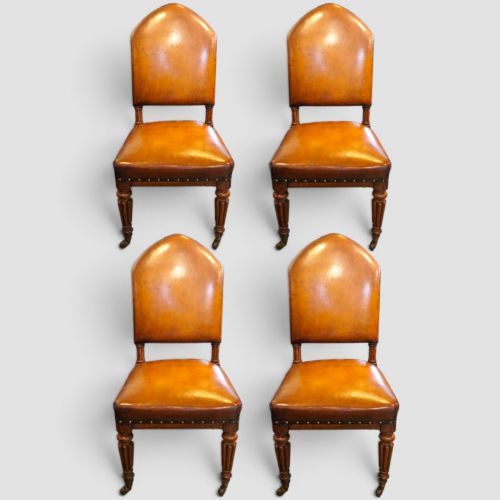 fig 4. A set of four Victorian oak dining chairs featuring arched gothic-style backrests upholstered in warm brown leather with brass stud trim.