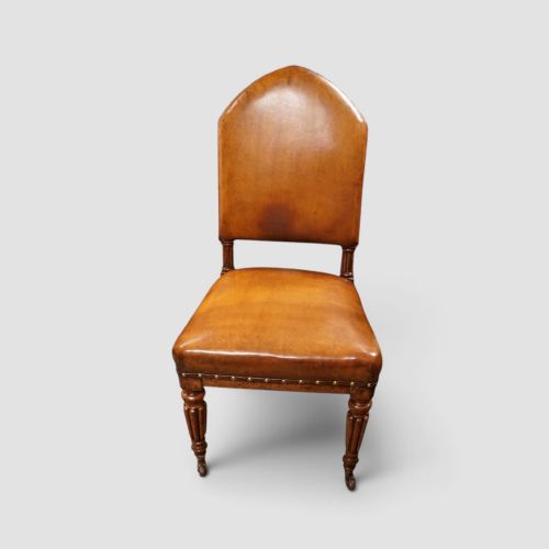 fig 6. A set of four Victorian oak dining chairs featuring arched gothic-style backrests upholstered in warm brown leather with brass stud trim.