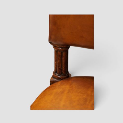 fig 7. A set of four Victorian oak dining chairs featuring arched gothic-style backrests upholstered in warm brown leather with brass stud trim.