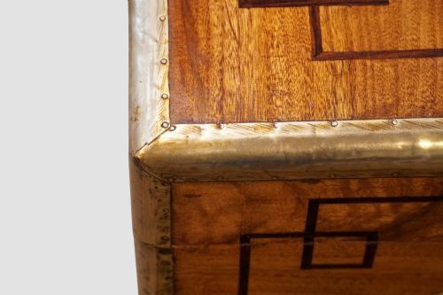 fig 1. A rectangular Victorian camphor wood campaign chest featuring polished brass binding along the edges, geometric dark line inlay, and a central brass lock escutcheon.