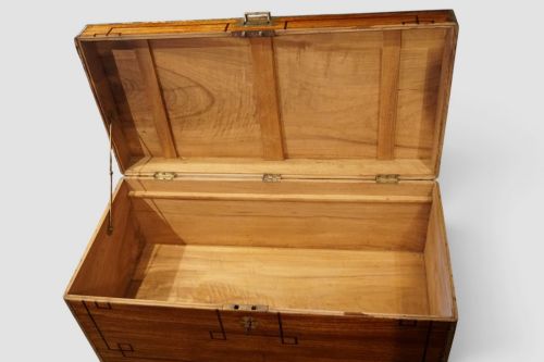 fig 8. A rectangular Victorian camphor wood campaign chest featuring polished brass binding along the edges, geometric dark line inlay, and a central brass lock escutcheon.
