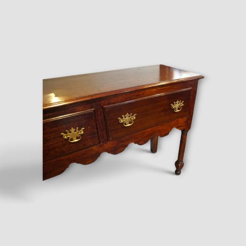 fig 1. An 18th-century George III dark oak dresser base featuring three drawers with brass handles and a scalloped apron on turned legs.