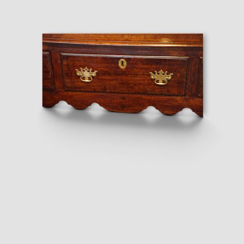 fig 5. An 18th-century George III dark oak dresser base featuring three drawers with brass handles and a scalloped apron on turned legs.