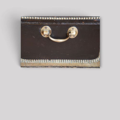 fig 8. An antique dark green leather trunk featuring brass corner straps, close-studded brass borders, and a brass keyhole escutcheon.
