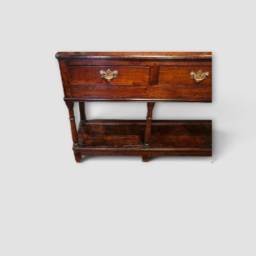 fig 2. An antique dark oak dresser base featuring three frieze drawers with brass handles supported by turned legs and a low open potboard shelf.