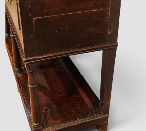 fig 4. An antique dark oak dresser base featuring three frieze drawers with brass handles supported by turned legs and a low open potboard shelf.