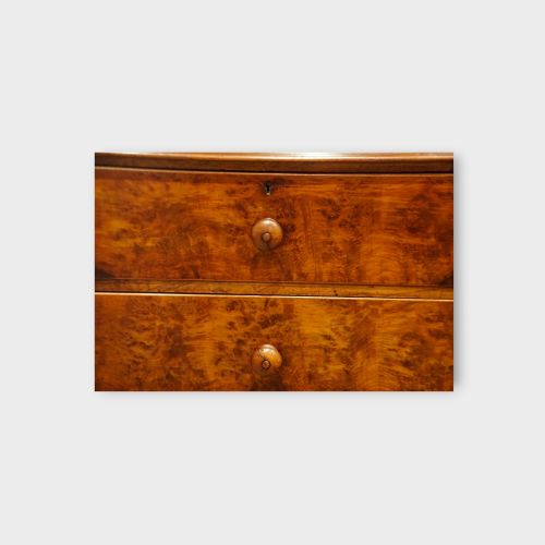 fig 6. A 19th-century Victorian burr walnut linen press featuring an upper cabinet with arched panel doors over a chest of four drawers with turned wooden knobs.
