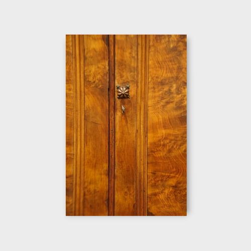 fig 7. A 19th-century Victorian burr walnut linen press featuring an upper cabinet with arched panel doors over a chest of four drawers with turned wooden knobs.