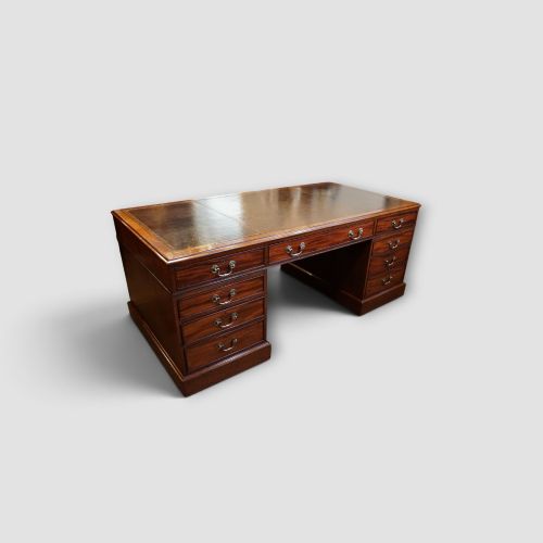 fig 1. A large Victorian mahogany partners desk featuring a brown leather inset writing surface, twin drawer pedestals, brass swan-neck handles, and a wide central kneehole.