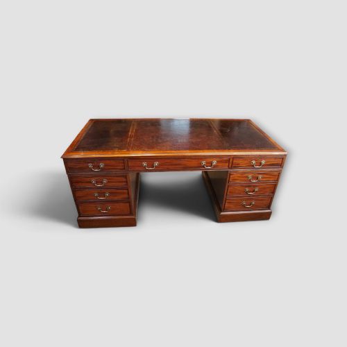 fig 4. A large Victorian mahogany partners desk featuring a brown leather inset writing surface, twin drawer pedestals, brass swan-neck handles, and a wide central kneehole.