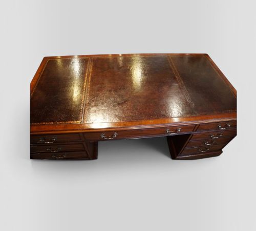 fig 6. A large Victorian mahogany partners desk featuring a brown leather inset writing surface, twin drawer pedestals, brass swan-neck handles, and a wide central kneehole.