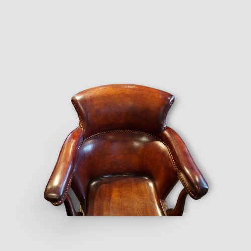 fig 2. An Edwardian mahogany and chestnut brown leather swivel desk chair with a curved tub backrest, brass stud detail, and a carved four-star base.